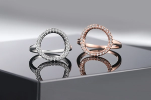 Macro detail of two rose gold and silver rings with zircon pavé on a black mirror