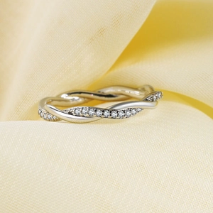 Elegante anillo plateado trenzado con circonitas brillantes sobre fondo de satén suave