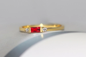 Macro shot of a 14K gold-plated geometric ring with emerald-cut red zircon and side stones
