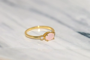 Detail of 14k gold plated ring featuring an oval pink gemstone and side zircon accents