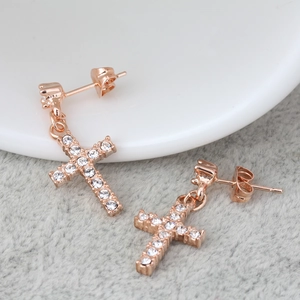 Orecchini a croce in oro rosa con zirconi incastonati su un piatto di ceramica