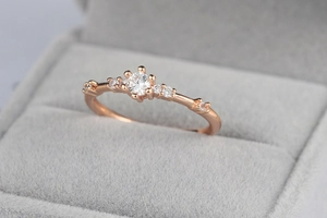 Macro view of rose gold engagement ring with round center stone and small side diamonds