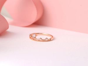 Close-up of rose gold crown ring with a sparkling zircon on a soft pink ribbon background