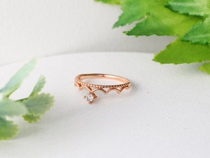 Detail shot of a rose gold crown ring with a hanging zircon on a decorative leaf background