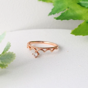 Elegant rose gold crown ring with sparkling zircon stone on a white textured surface