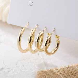 Macro detail of two pairs of minimalist gold hoop earrings on a white jewelry card display