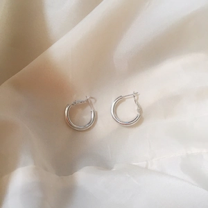 Macro shot of polished silver hoop earrings on champagne silk fabric background