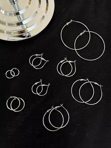Flat lay of multiple sizes silver hoop earrings on a textured black background