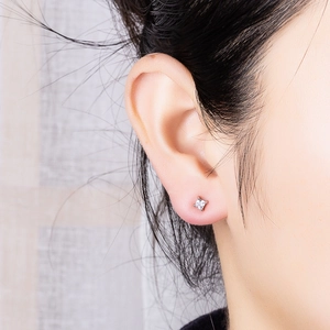 Close-up of a square-cut zircon stud earring with a four-claw silver setting on an ear