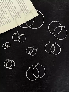 Multiple sizes of polished silver hoop earrings arranged on a textured black background