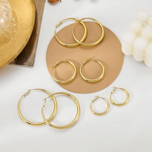 Set of four gold hoop earrings in various sizes displayed on a minimalist white surface