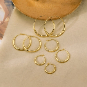 Detailed arrangement of five polished gold hoop earrings on a soft fabric background