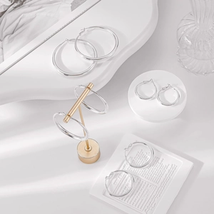 Set of four varying sized silver hoop earrings displayed on elegant jewelry stands