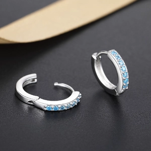 Macro detail of silver hinged hoop earrings featuring sky blue zirconia stones on black