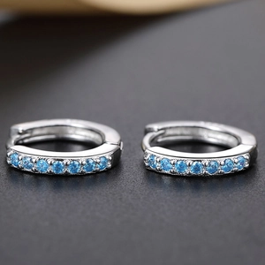 Detailed close-up of silver huggie earrings with light blue crystals on a dark background