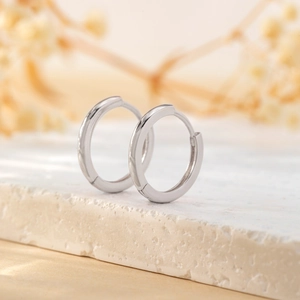 Minimalist silver huggie hoop earrings displayed on a white textured stone surface
