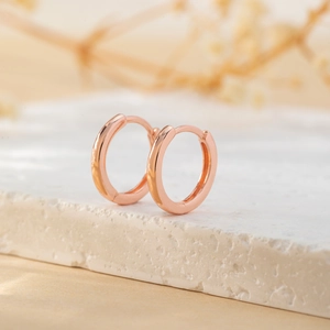 Detailed close-up of rose gold huggie hoop earrings on a textured stone display