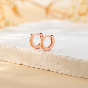 Close-up of minimalist rose gold huggie hoop earrings on a textured stone pedestal