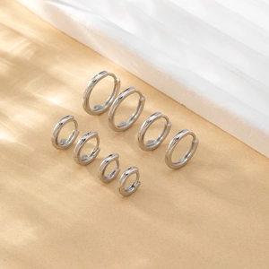 Set of four different sized silver polished hoop earrings on a textured beige background