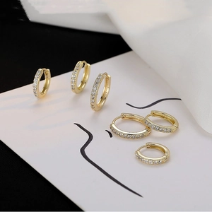 Three sizes of gold hoop earrings with white zircon stones on a minimalist art card