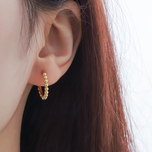 Minimalist golden beaded hoop earrings with a textured surface shown on a female ear