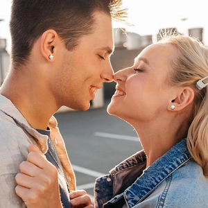 Close-up of sparkling round zircon stud earrings worn by a couple in sunset light