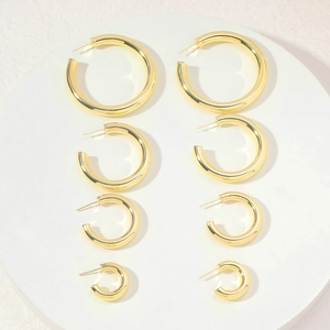 Set of four polished gold hollow C-shaped earrings in various sizes on a white tray