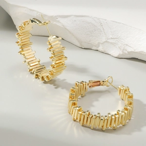 Detail view of gold layered geometric hoop earrings resting on a white mineral stone