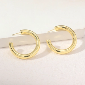 Close-up of chunky gold hollow C-shape hoop earrings on a textured minimalist background