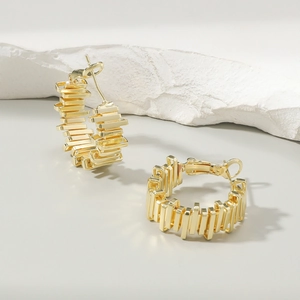 Macro detail of golden geometric loop earrings with vertical line texture on stone base