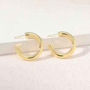 Close-up of polished gold C-shape hoop earrings on a textured minimalist background