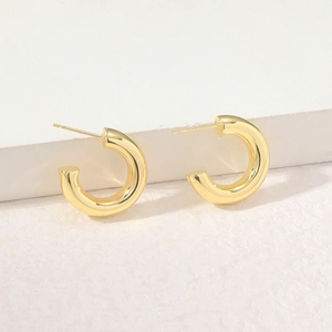 Detail view of glossy gold-plated hollow C-shape earrings on a white textured stone base