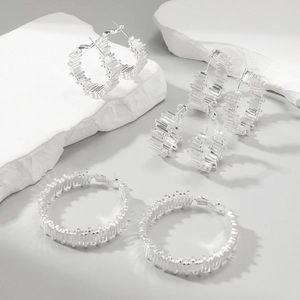 Three-piece set of irregular silver geometric hoop earrings on a minimalist stone background