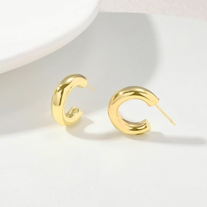 Macro detail of polished gold C-shape hoop earrings on a minimalist white tray