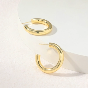 Close-up of golden hollow C-shape earrings on a minimalist white circular display stand