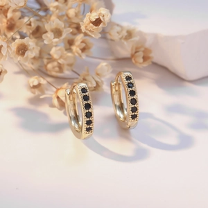 Gold hoop earrings with black zircon pavé and beaded edges on a minimalist background