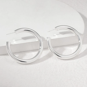 Macro shot of polished silver 925 needle C-shape hoop earrings on a marble stone base
