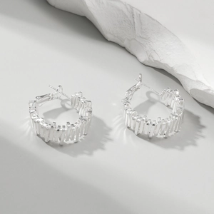 Detail of silver hoop earrings featuring irregular geometric stacked textures and polished finish