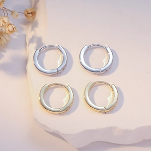 Elegant gold and silver hoop earrings with black zircon stones on stone display base