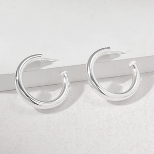 Polished silver C-shape hoop earrings displayed on white geometric stones