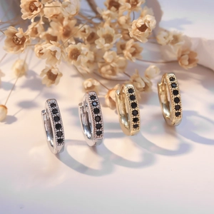 Hoop earrings in gold and silver with black zircon stones and beaded edges on white background
