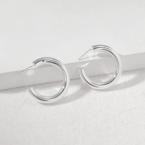 Close-up of chunky silver C-shape hoop earrings on a textured stone display