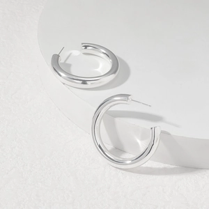 Detailed macro view of high-polished silver hollow C-shaped hoop earrings on a white podium