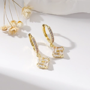 Elegant gold earrings with sparkling zircon pendant on a white surface, professional jewelry shot