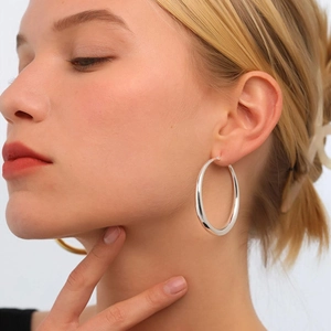Close-up of a model wearing large polished silver hoop earrings with a sleek metallic finish