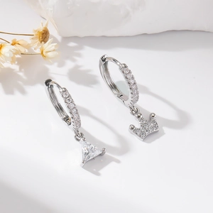 Silver asymmetrical hoop earrings with triangle zircon and crown pendants on a marble base