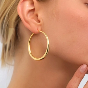 Close-up of polished gold-finish large hoop earrings worn on a model with sleek modern style