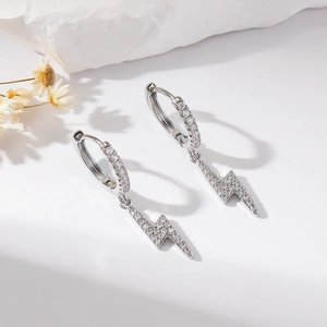 Detail of silver lightning bolt earrings with clear cubic zirconia on a white stone