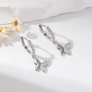 Detail of silver butterfly earrings with sparkling cubic zirconia on white stone surface