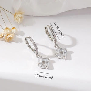 Close-up of silver earrings with hollow square pendants and sparkling zircon stones